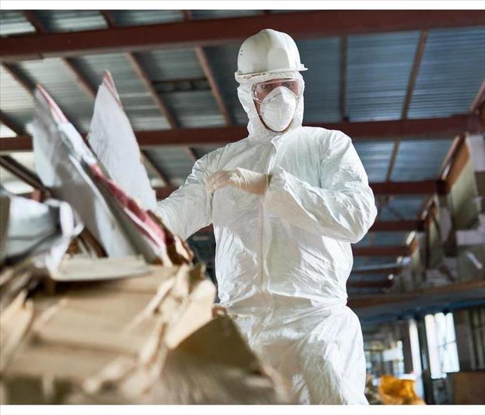Low angle portrait of factory worker wearing biohazard suit sorting reusable cardboard on waste processing plant,